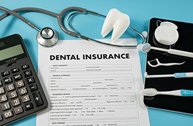 Dental insurance form next to calculator and dental instruments