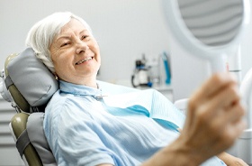 Senior woman using mirror to admire her implant dentures