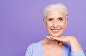 Smiling woman with dental implants in Branford on purple background
