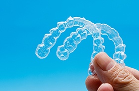 Hand holding two clear aligners against blue background