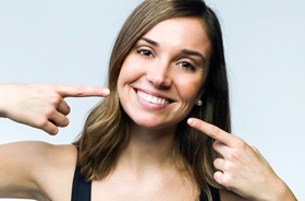 Woman pointing at her perfect teeth, happy she could afford veneers
