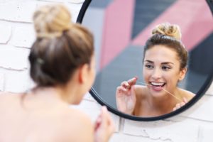 Woman standing in front of mirror, flossing with Invisalign in Branford