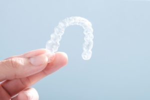 Hand holding Invisalign aligner against neutral background